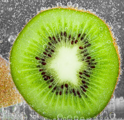 Bubbles on a kiwi segment in soda water on blue background