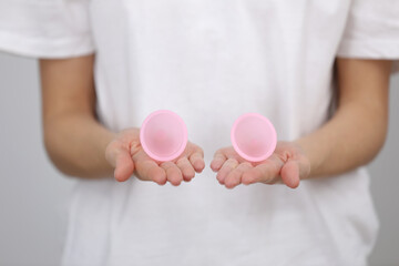 close up of woman holding pink menstrual cups of different size in her hands on white background. Gynecology concept