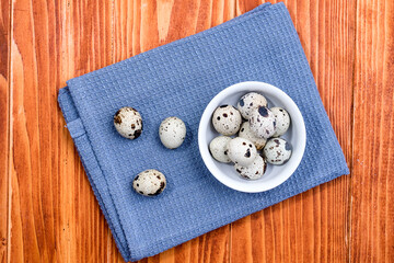 Quail eggs in white ceramic bowl on blue kitchen cloth. Top view. Detailed closeup of spotted quail eggs, rustic wooden background