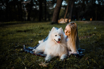 beautiful woman in white shirt is resting on the grass with her white dog samoyed outdoors in the park.