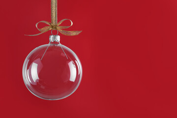 Transparent glass Christmas ball with golden ribbon and bow against red background. Space for text