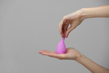 Young woman hand holding a pink menstrual cup - gray background. Gynecology concept