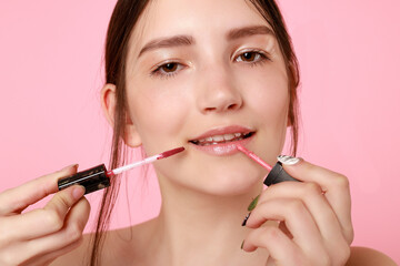 Closeup of lovely young girl with natural nude makeup posing on pink isolated background in studio. Charming female with lip gloss looking down and smiling. 16:9 panoramic format.