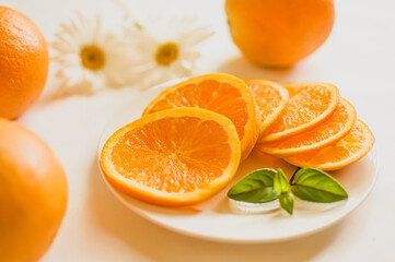 Fototapeta na wymiar cut orange on a white plate and white flowers on the background