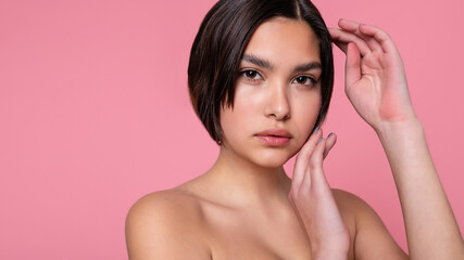 Close up face of beautiful young woman with clean perfect skin. Portrait of beauty model with natural nude make up. Spa, skin care and wellness. Pink peach coral background. 16:9 panoramic format.