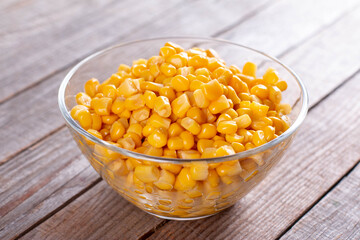 Sweet marinated corn seeds in glass bowl on wooden table
