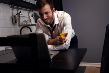 Portrait of businessman at home resting after long day at work having video call at kitchen using laptop.