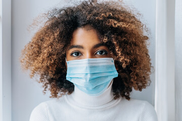 Portrait of an African-American girl in a protective medical mask close-up looks at the camera, protection from the coronavirus pandemic