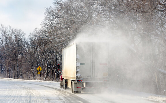 A Semi -truck Travels Down Icy Slick Roads In Michigan, With Blowing Snow Falling Off The Roof
