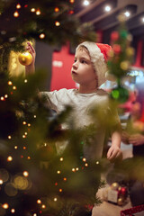 A little boy who hangs decorations on the Christmas tree at home. Together, New Year, family, celebration