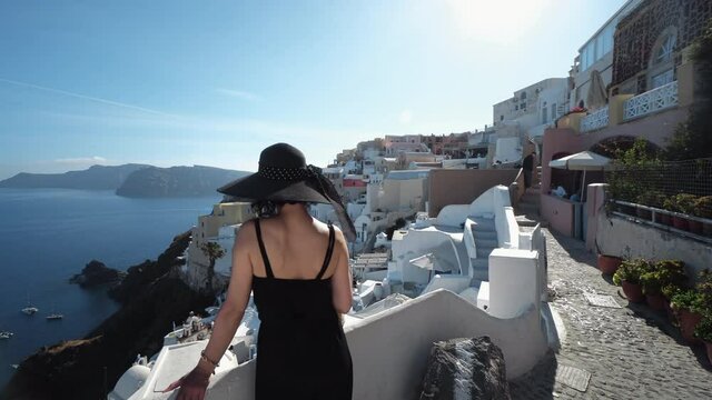 elegant brunette woman in black standing by the wall enjoying amazing santorini panoramic view of oia