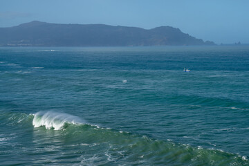 large waves on the coast of Galicai with fishing boat and mountain behind