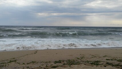 The waves at sea are not a formidable element.
Bulgaria. Black Sea. Deserted sandy beach under a gray-blue sky. Large sea waves run ashore. The water under the sky is gray-blue. A lonely trail runs al