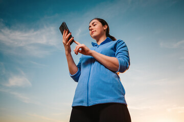 A young woman uses a smartphone. Bottom view. The sky is in the background. Concept of modern technologies