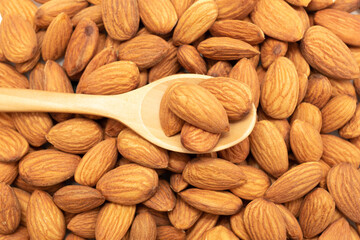 The almonds are in a brown wooden spoon and several seeds around.