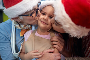 Fototapeta premium A little girl posing for a photo being kissed by grandma and mother on a Xmas. Christmas, family, together