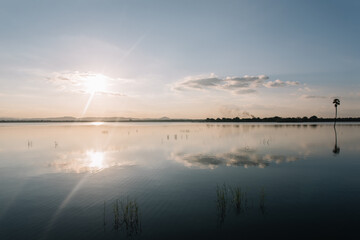 reflective lake pond water by the sea shows mirror image of the skyline sun trees and clouds. Blue skys summer in sri lanka