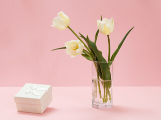 Bouquet of yellow tulips in vase with gift box on a pink background.