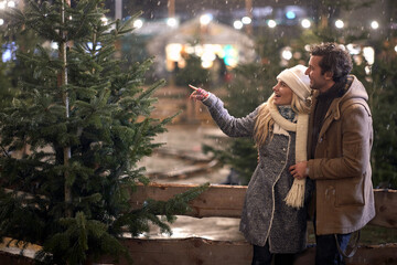 Obraz premium A young couple in love watching a christmas tree on a snowy night in the city. Christmas tree, love, relationship, Xmas, snow