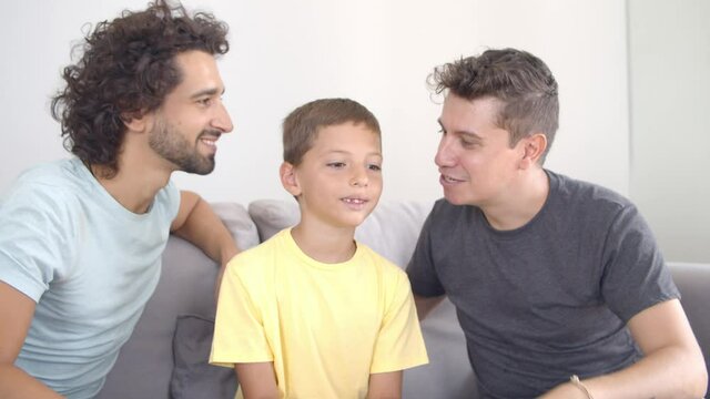 Two happy dads kissing son. Family sitting on couch, enjoying time together. Front view. Parenthood and love concept