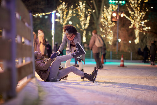 A young guy falling down at skating at ice rink. Skating, closeness, love, together