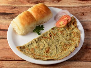 Indian Masala Egg Omelet, made with fresh vegetables tomato,onion, hot chili pepper, parsley.. served with pav bread on rustic wooden background, selective focus