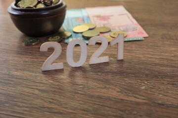 Letters on the number 2021 with a pile of coins and banknotes on wooden background 