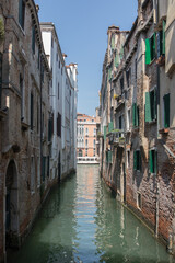 Fototapeta na wymiar river canal view from bridge boat in venice italy during summer with buildings to each side colourful water blue skies green windows