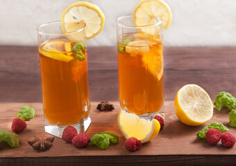 Two glasses with kombucha, drinking straws and lemon slices, raspberries are on a wooden table.