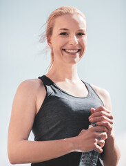 Junge, attraktive Frau in Sportkleidung hält eine Wasserflasche und lächelt in die Kamera