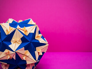 Close up view blue and cream star pattern Kusudama origami ball on a bright pink background