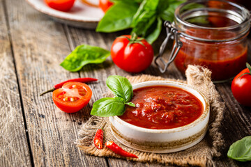 Bowl of italian tomato sauce with basil and fresh tomatoes on wooden background