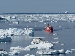 A red and white ship navigates its way between melting  drifting ice floes.Ice bergs can be seen on the horizon.Climate change crisis and emergency © Tony Skerl