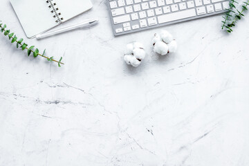 Laptop, cotton branch, notebook on white stone background flat lay copy space. freelancer, blogger home desk workspace.