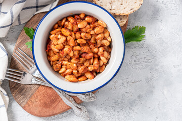 White beans with spicy tomato sauce in a bowl on a gray concrete table top view. Greek style food, Mediterranean cuisine. Tasty vegetarian food with white beans.