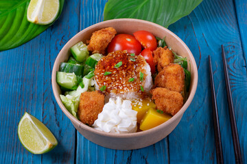 Poke bowl with fried chicken, vegetables and rice on the blue wooden table. Hawaiian cuisine meal