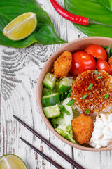 Poke bowl with fried chicken, vegetables and rice on the white wooden table. Hawaiian cuisine meal
