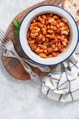 White beans with spicy tomato sauce in a bowl on a gray concrete table top view. Greek style food, Mediterranean cuisine. Tasty vegetarian food with white beans.