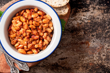 White beans with spicy tomato sauce in a bowl on a dark background top view. Greek style food, Mediterranean cuisine. Tasty vegetarian food with white beans.