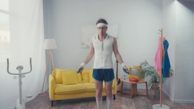 Energetic sportsman jump roping in living room, retro sport concept