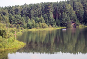 Summer landscape: a forest lake, the reflection of trees in the water, people in a boat and a mother with a child.