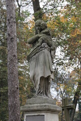 a cemetery monument, a sculpture of a woman with a child in a tomb, among the trees