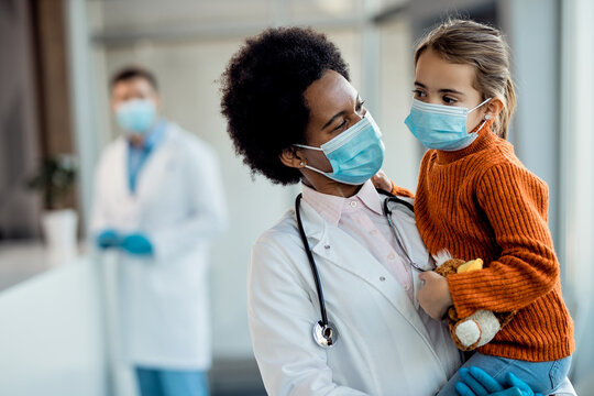 African American pediatrician and small girl with protective face masks at medical clinic.