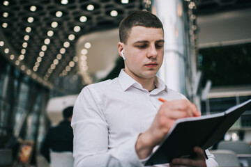 Serious entrepreneur in wireless earphones taking notes in planner