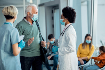 Obraz premium African American doctor and senior man communicating in a hallway while wearing face masks.