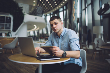 Fototapeta na wymiar Pensive man with clipboard and laptop working in cafe