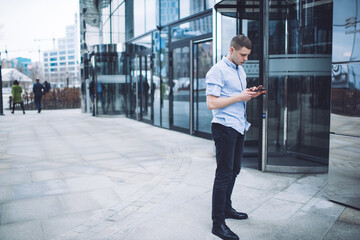 Concentrated man browsing smartphone near business center entrance