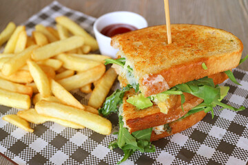 Closeup grilled chicken avocado salad sandwich and french fries on checker paper