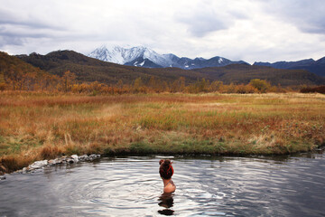 Young woman with dreadlocks is resting in hot thermal springs, admiring the autumn taiga and volcanoes. Kamchatka, Nalychevo springs