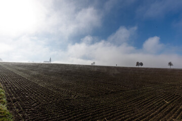 Auflösender Nebel über gepflügtem Acker mit Blauem Himmel 